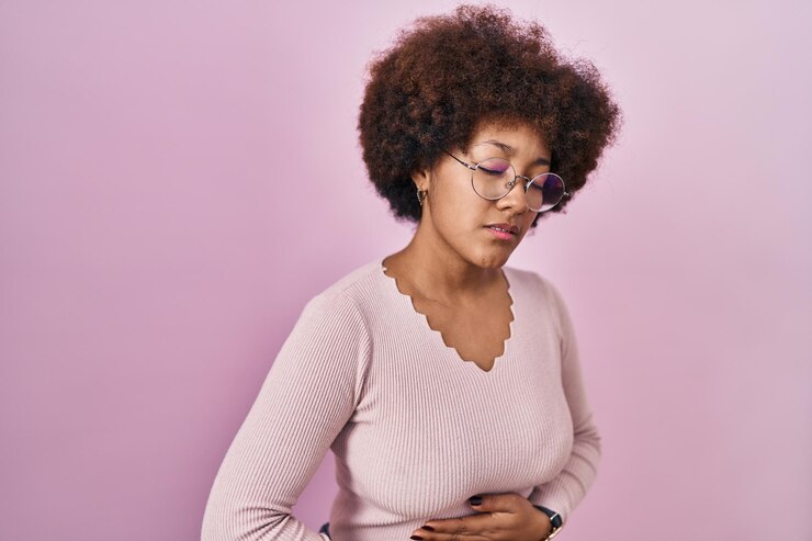 Foto grátis jovem mulher afro-americana em pé sobre fundo rosa com a mão no estômago porque indigestão, doença dolorosa se sentindo mal. conceito de dor.