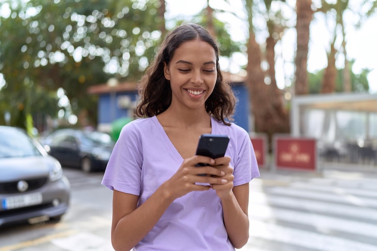 Foto grátis jovem mulher afro-americana sorrindo confiante usando smartphone na rua