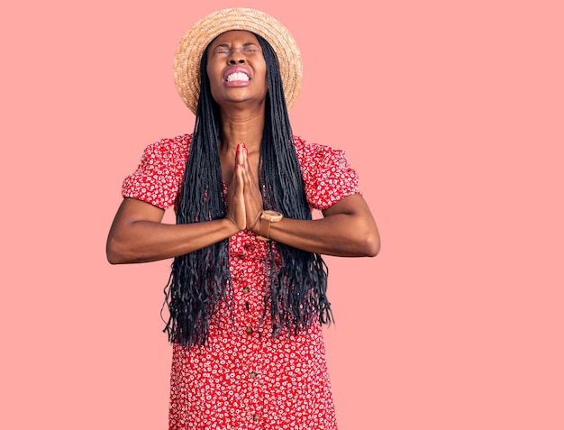 Foto grátis jovem mulher afro-americana usando chapéu de verão implorando e rezando com as mãos junto com a expressão de esperança no rosto muito emocionada e preocupada implorando