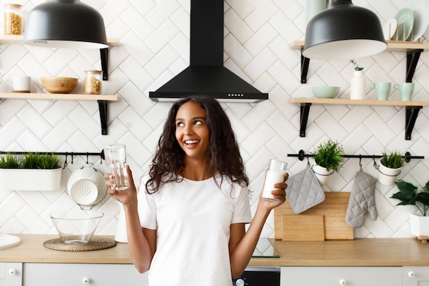 Jovem mulher afro tem dois copos com água e leite