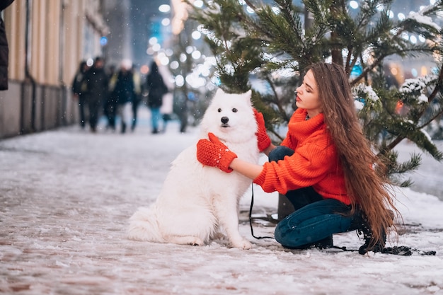 Jovem mulher agachada ao lado de um cachorro em uma rua de inverno