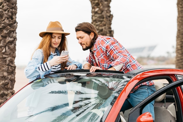 Foto grátis jovem mulher alegre com smartphone perto de homem, inclinando-se para fora do carro