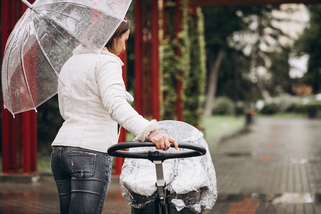 Jovem mulher andando com carrinho de bebê sob o guarda-chuva em um tempo raint