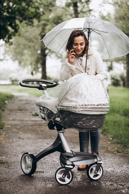 Jovem mulher andando com carrinho de bebê sob o guarda-chuva em um tempo raint