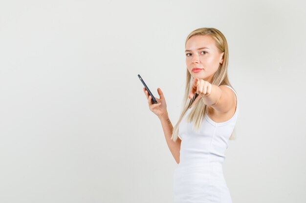 Jovem mulher apontando o dedo para a câmera com smartphone em camiseta