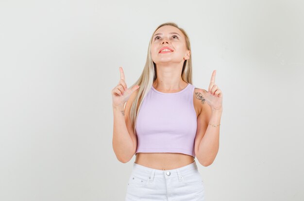 Jovem mulher apontando o dedo para cima em camiseta, minissaia e parecendo alegre