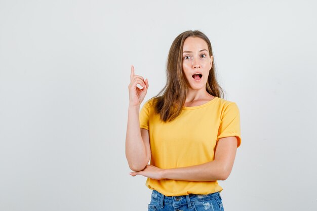 Jovem mulher apontando o dedo para cima em uma camiseta, shorts e parecendo surpresa