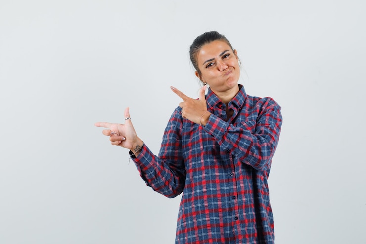 Foto grátis jovem mulher apontando para a esquerda com o dedo indicador e bochechas estufadas em camisa xadrez e parecendo feliz. vista frontal.