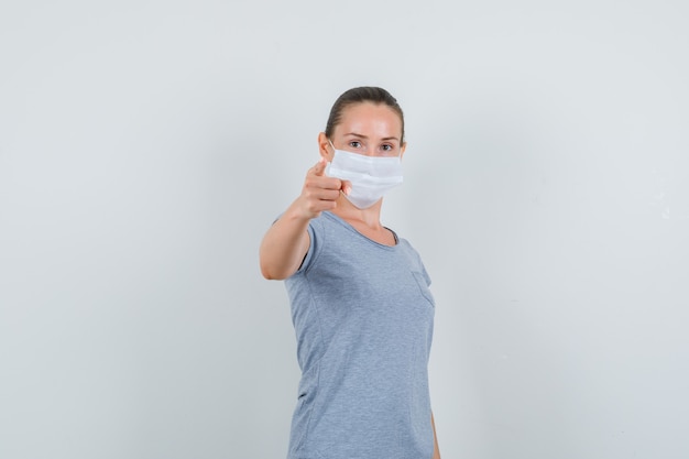 Jovem mulher apontando para a frente em t-shirt, máscara, vista frontal.