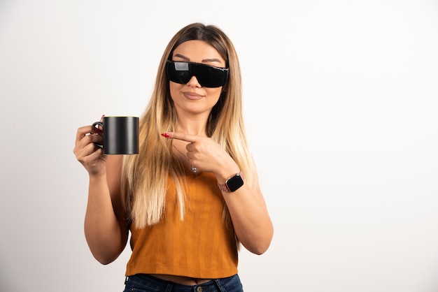 Jovem mulher apontando para a xícara preta e usando óculos de proteção.