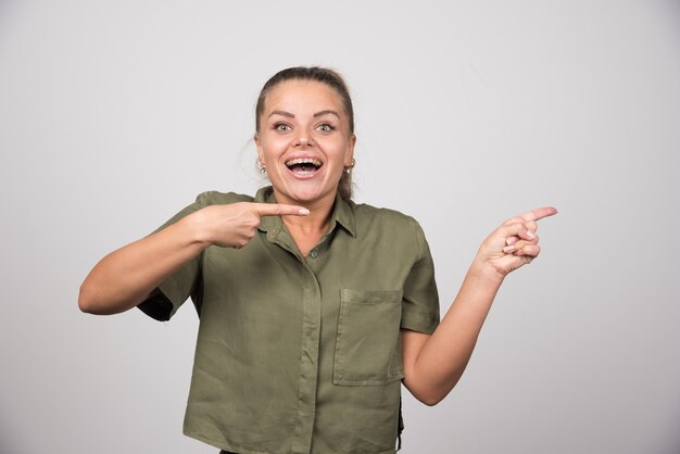 Jovem mulher apontando para algo na parede cinza.