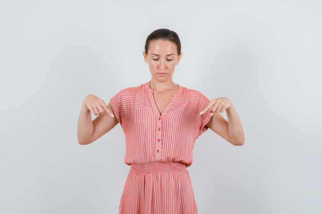 Jovem mulher apontando para baixo em um vestido listrado e olhando com foco, vista frontal.