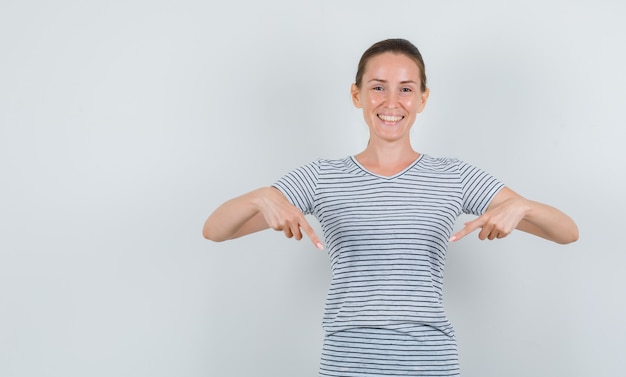 Foto grátis jovem mulher apontando para baixo em uma camiseta e olhando alegre, vista frontal.