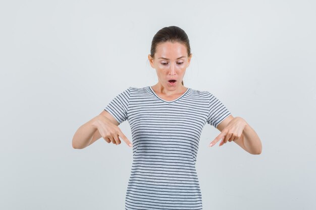 Jovem mulher apontando para baixo em uma camiseta e parecendo surpresa. vista frontal.