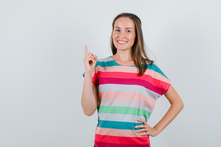 Foto grátis jovem mulher apontando para cima em t-shirt e olhando feliz. vista frontal.