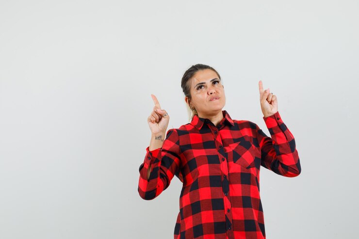 Foto grátis jovem mulher apontando para cima na camisa e olhando esperançosa, vista frontal.