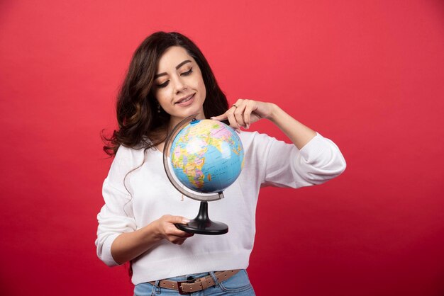 Jovem mulher apontando para o globo sobre fundo vermelho. Foto de alta qualidade