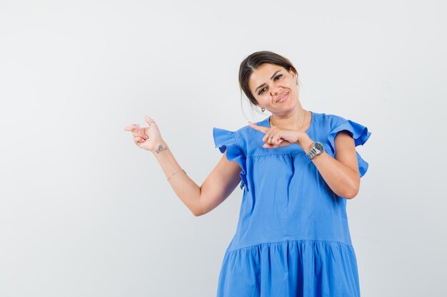 Jovem mulher apontando para o lado com um vestido azul e parecendo alegre