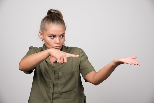 Jovem mulher apontando para o lado dela na parede cinza.