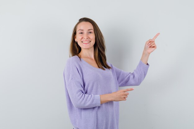 Jovem mulher apontando para o lado enquanto sorria com uma blusa lilás e parecia alegre. vista frontal.