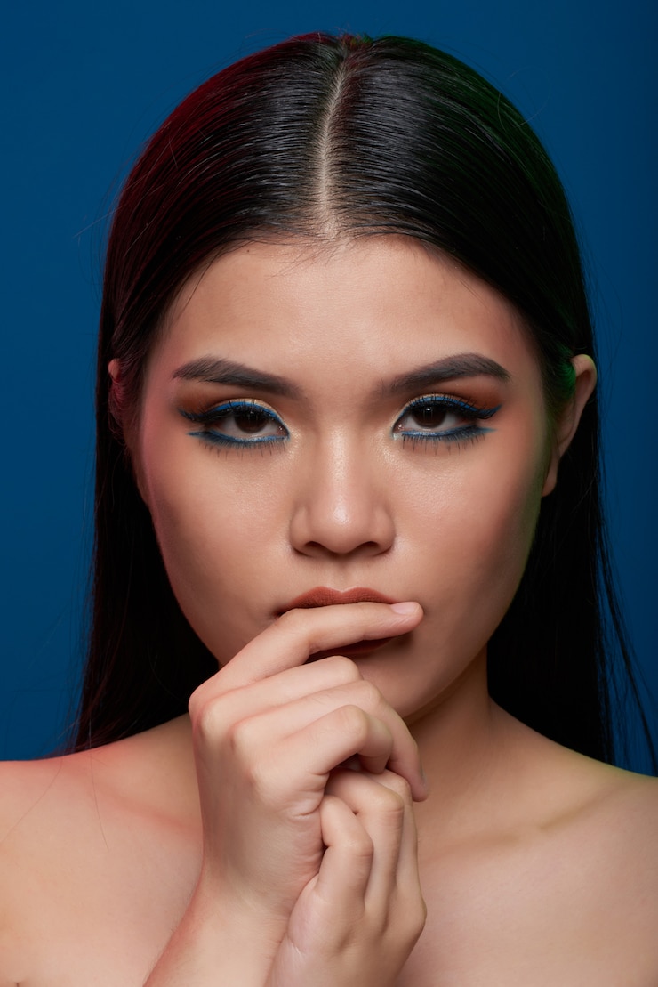 Foto grátis jovem mulher asiática com maquiagem completa e ombros nus, tocando os lábios e olhando para a câmera