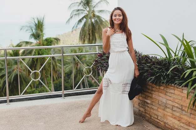 Foto grátis jovem mulher asiática elegante com vestido boho branco, estilo vintage, natural, sorridente, feliz, férias tropicais, hotel, fundo de palmeiras