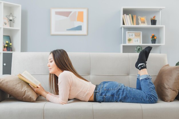 Jovem mulher asiática em roupas casuais, deitada em um sofá em casa lendo livro feliz e positivo relaxante passando o fim de semana em casa