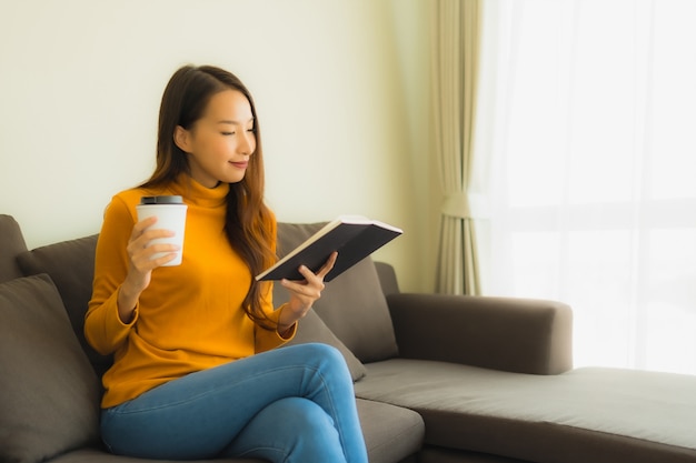 Jovem mulher asiática retrato ler livro na cadeira do sofá com travesseiro na sala de estar