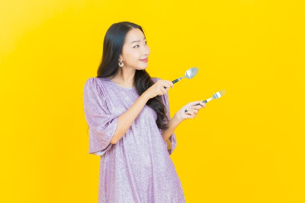 jovem mulher asiática sorrindo com colher e garfo amarelo