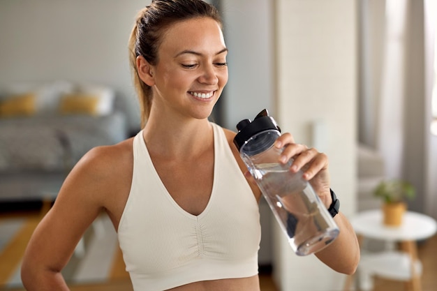 Jovem mulher atlética feliz bebendo água após o exercício em casa
