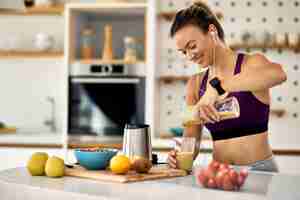 Foto grátis jovem mulher atlética feliz tomando um smoothie de frutas no café da manhã na cozinha