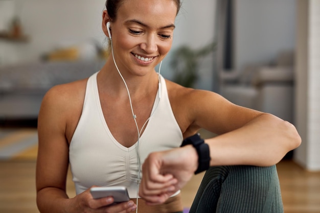 Jovem mulher atlética feliz verificando o tempo no relógio de pulso após o exercício em casa