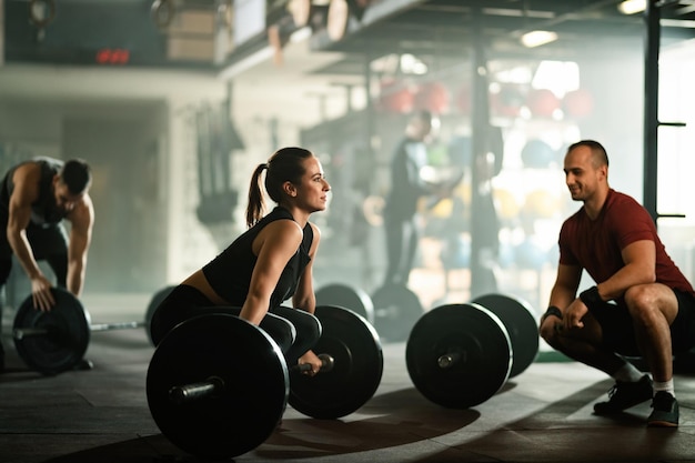 Jovem mulher atlética levantando a barra enquanto faz treinamento de força com seu instrutor em uma academia