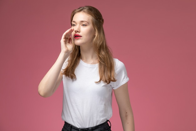 Jovem mulher atraente em uma camiseta branca posando de frente e chamando na parede rosa modelo feminino pose foto colorida