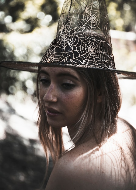 Jovem mulher atraente no chapéu de bruxa na floresta murcha