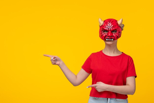 Jovem mulher atraente usando máscara de diabo assustadora fundo amarelo garota de halloween