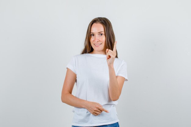 Jovem mulher avisando alguém com gesto de dedo em t-shirt branca, vista frontal de shorts.