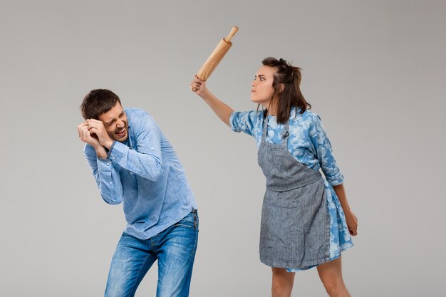 Jovem mulher batendo em homem com rolo sobre fundo cinza