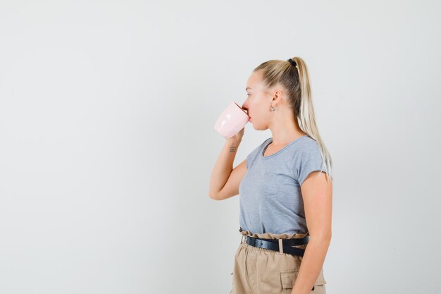 Jovem mulher bebendo café em t-shirt, calças e elegante. vista frontal.