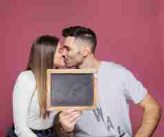 Foto grátis jovem mulher beijando com homem positivo e mostrando o frame da foto