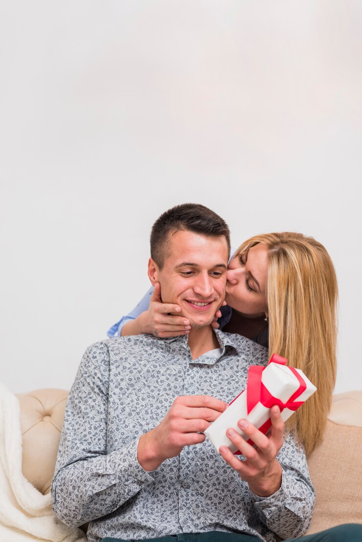 Foto grátis jovem mulher beijando homem sorridente com presente no sofá