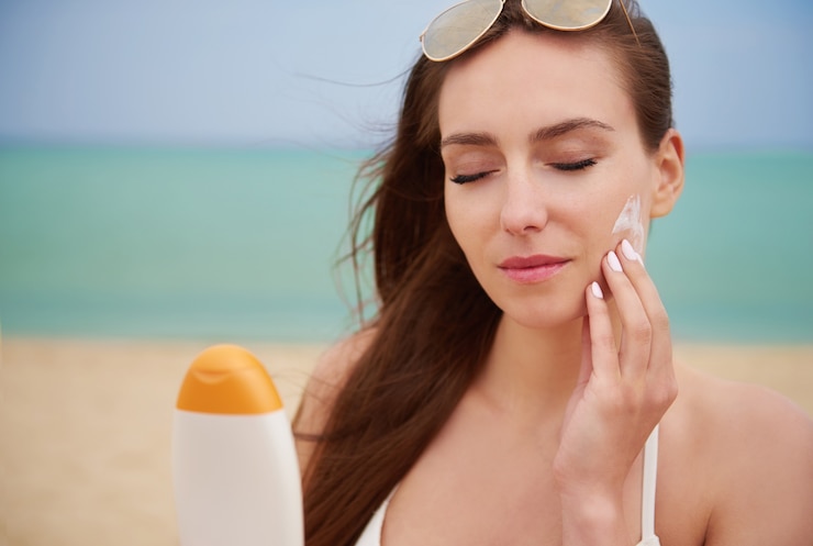 Foto grátis jovem mulher bonita a aplicar creme solar na praia.