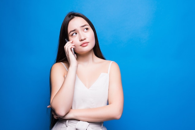 Jovem mulher bonita asiática falando no celular, isolada sobre a parede azul