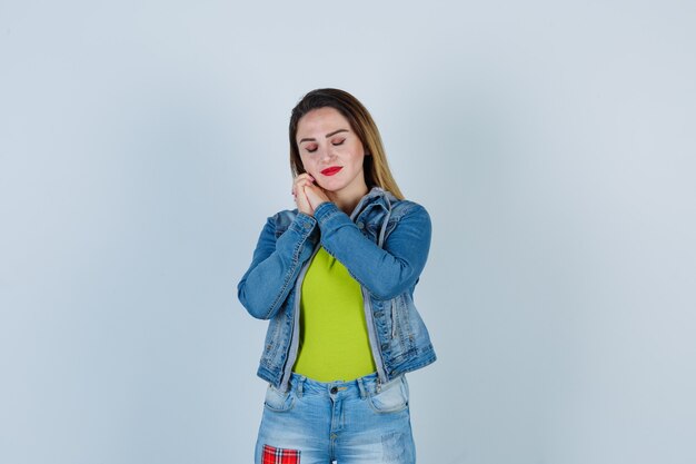 Jovem mulher bonita com as mãos perto do rosto em roupa jeans e olhando relaxado, vista frontal.