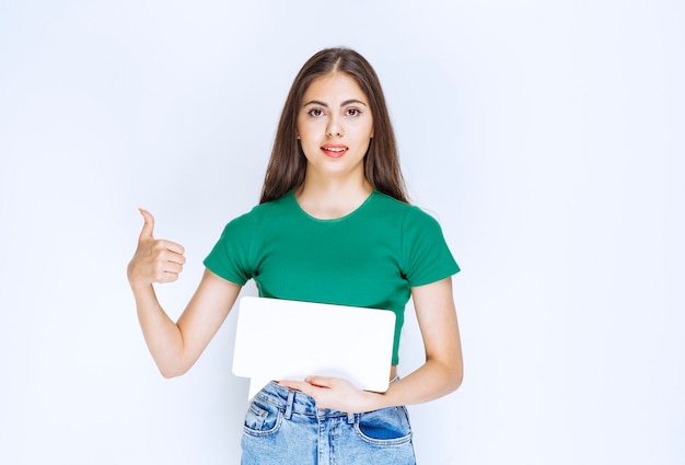 Jovem mulher bonita com camisa verde, mostrando o quadro de discurso em branco sobre fundo branco.