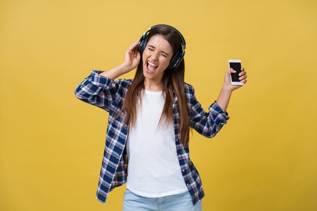 Jovem mulher bonita com fones de ouvido, dançando e cantando, isolados em fundo amarelo.