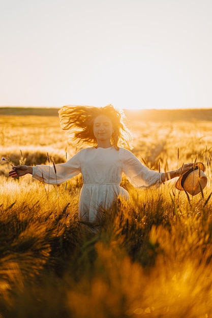 jovem mulher bonita com longos cabelos loiros em um vestido branco em um campo de trigo no início da manhã ao nascer do sol. O verão é a hora dos sonhadores, cabelos voadores, uma mulher correndo pelo campo nos raios