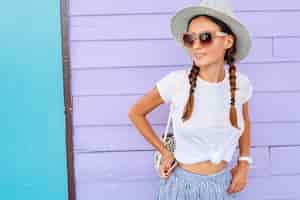 Foto grátis jovem mulher bonita com roupa de moda verão estilo casual, posando contra uma parede colorida, viajando, chapéu, óculos de sol, sorrindo, feliz