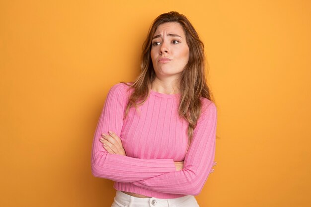 Jovem mulher bonita com top rosa olhando de lado descontente com os braços cruzados