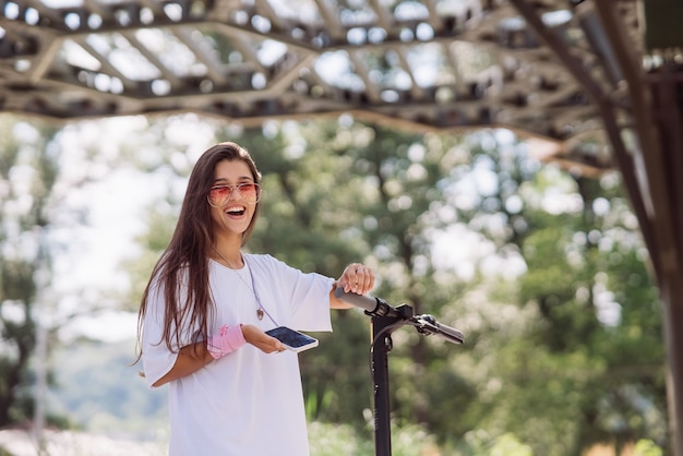 Jovem mulher bonita e scooter elétrica no parque de transporte ecológico